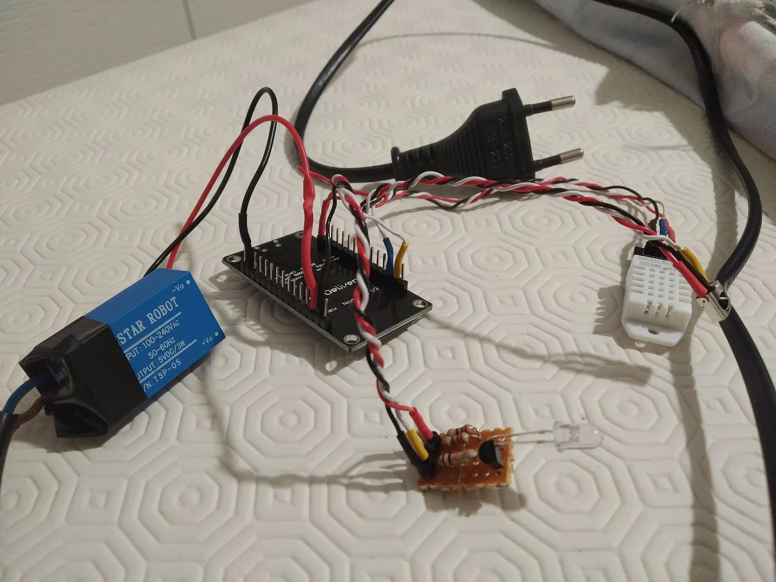 The components spread out: the mains-to-5V module labelled 100-240VAC to 5VDC, the ESP8266 board in the middle, the small soldered board with its infrared LED, and a white temperature and humidity sensor on a long twisted lead at the right