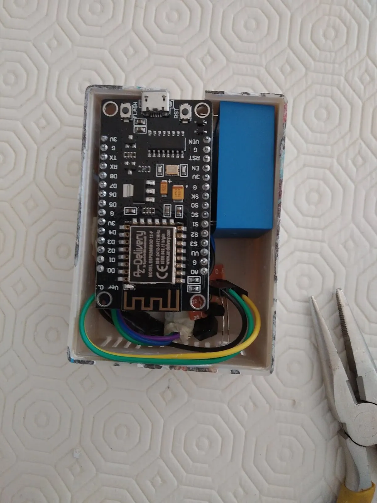 The inside of a small white plastic enclosure: an ESP8266 development board fills most of it, with the blue mains-to-5V module standing alongside and coloured wires tucked underneath