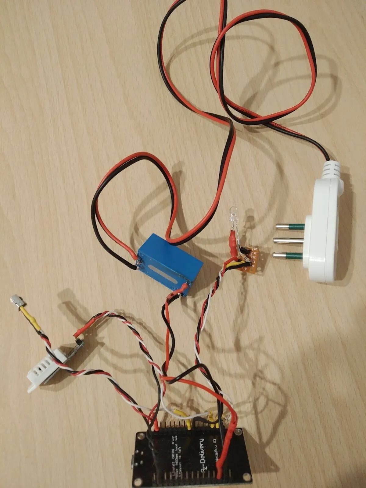 The finished assembly laid out on a table: a blue mains-to-5V module, the small soldered board with the infrared LED standing off it, a temperature sensor on a lead, a mains plug, and the ESP8266 board, all wired together